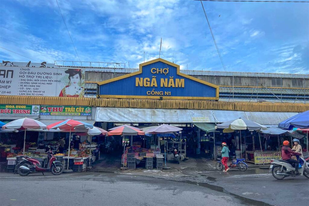 Main entrance of Nga Nam Central Market with signboard and motorbikes outside.