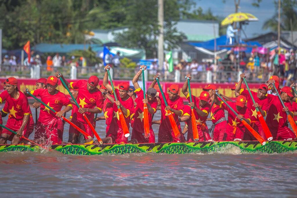 Khmer rowing team in red uniforms with golden star paddling together during the Ghe Ngo Boat Race Festival in Soc Trang, Vietnam.