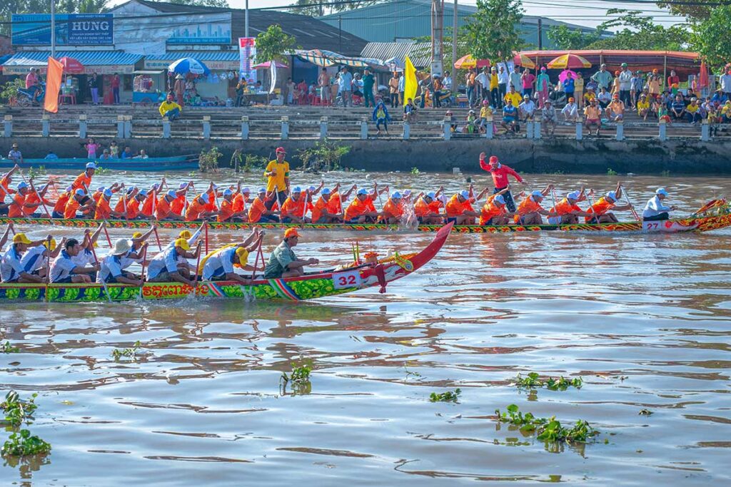 Colorful Khmer longboats racing on the Maspero River during the Ghe Ngo Boat Race Festival in Soc Trang, Vietnam, with rowers paddling in unison to cheers from the crowd.