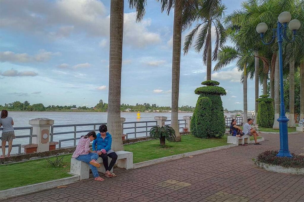 Nguyen Du Park riverside promenade in Long Xuyen – Locals relaxing under palm trees by the Hau River at Nguyen Du Park.