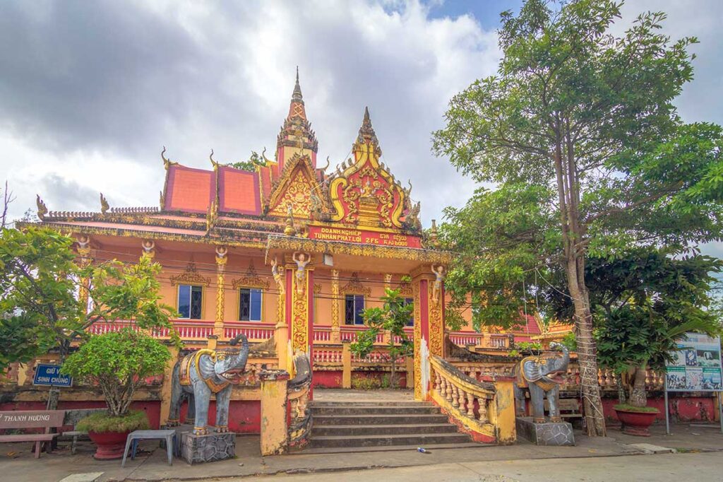Khmer-style main hall at Som Rong Pagoda, with red roof, golden trim, and elephant statues guarding the staircase