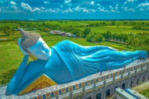 Closer aerial view of the reclining Buddha statue at Som Rong Pagoda, showing its serene face and raised platform with visitors walking along