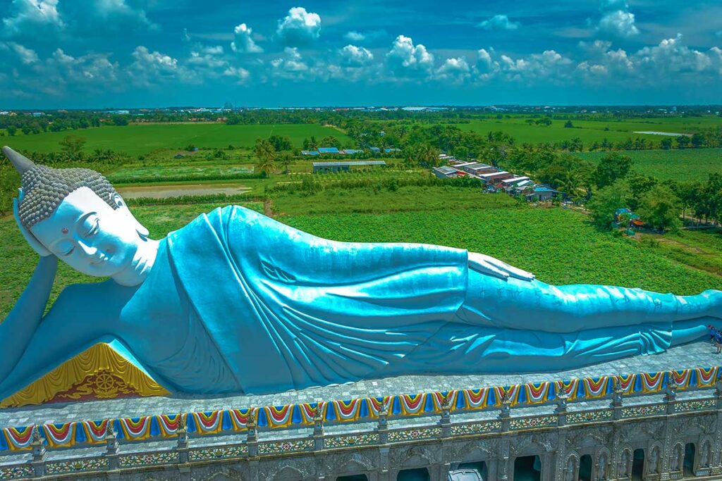 Side view of the reclining Shakyamuni Buddha statue at Som Rong Pagoda, set against green Mekong Delta rice fields