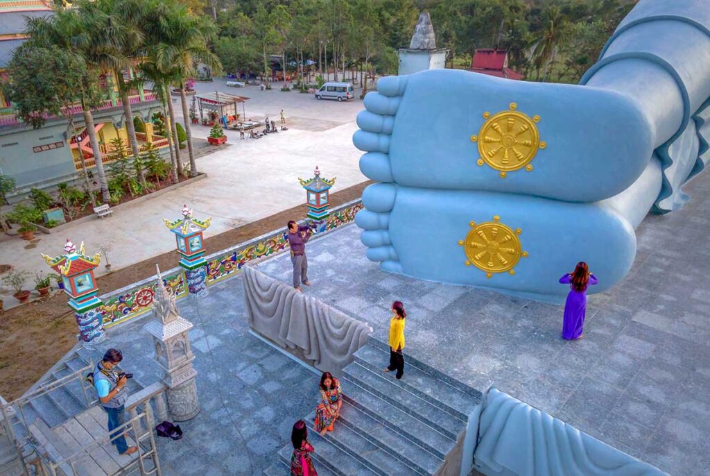 Close-up of the giant reclining Buddha’s feet at Som Rong Pagoda, decorated with golden dharma wheel symbols, with visitors taking photos