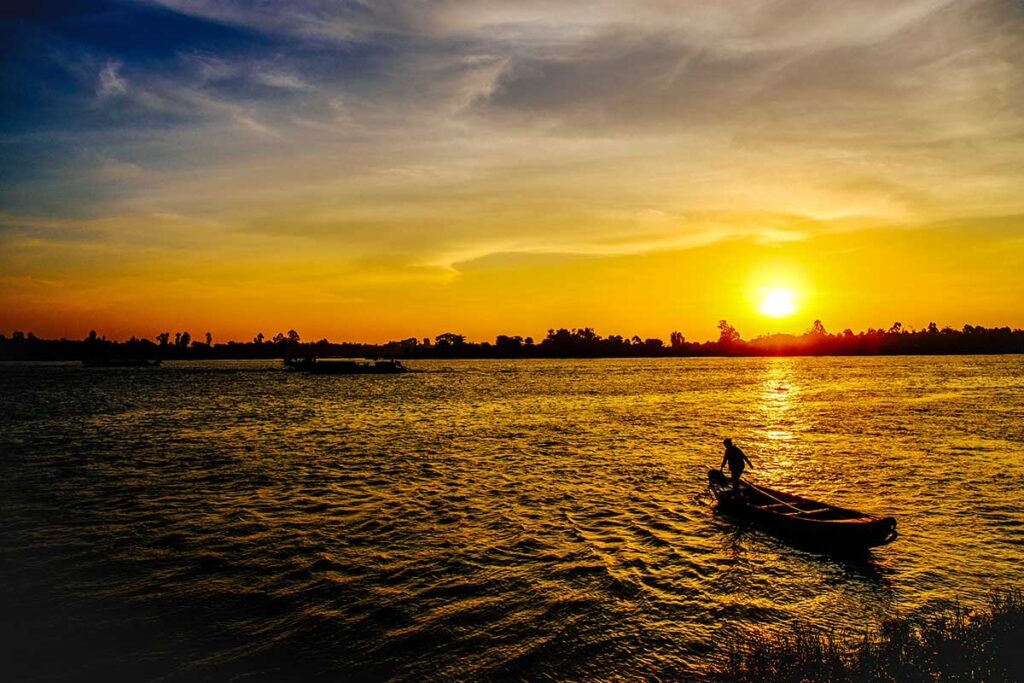 Sunset over Hau River in Long Xuyen – Golden evening light with silhouette of a fisherman rowing a small boat on the Hau River.