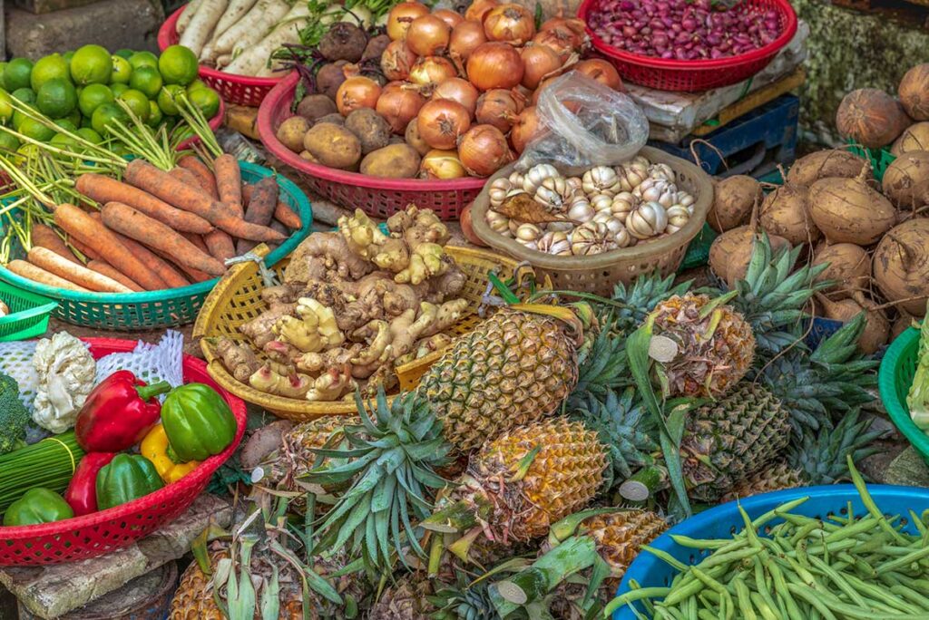 Close-up of colorful fruits and vegetables at Tân An Market in Cần Thơ including pineapples, ginger, onions, and bell peppers.