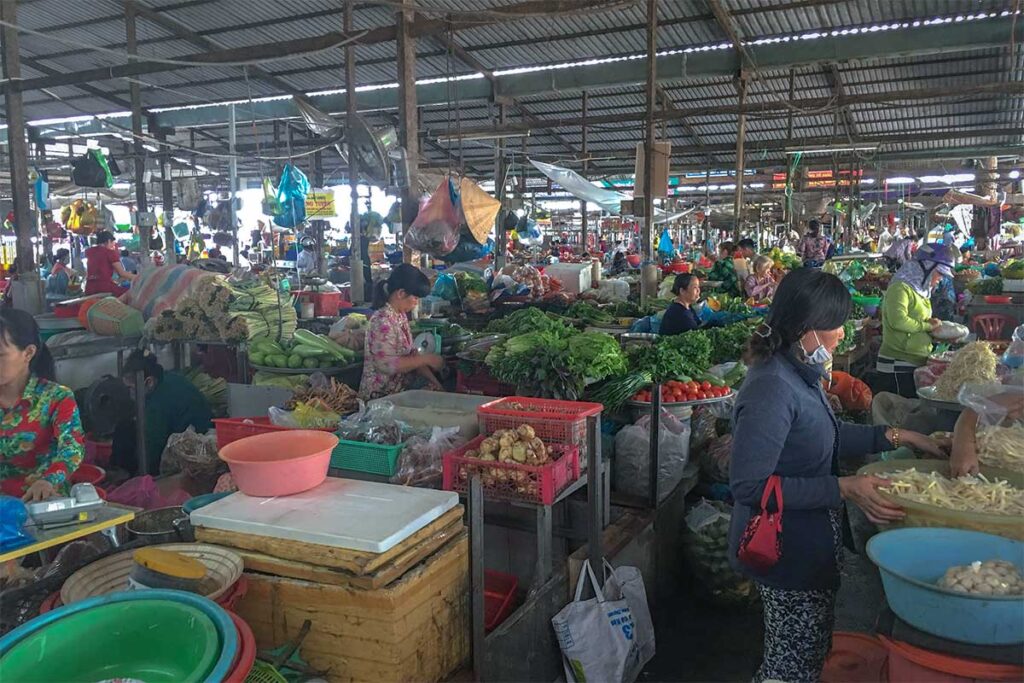 Vegetable stalls inside Tân An Market in Cần Thơ selling leafy greens, herbs, and root vegetables under the covered market roof.