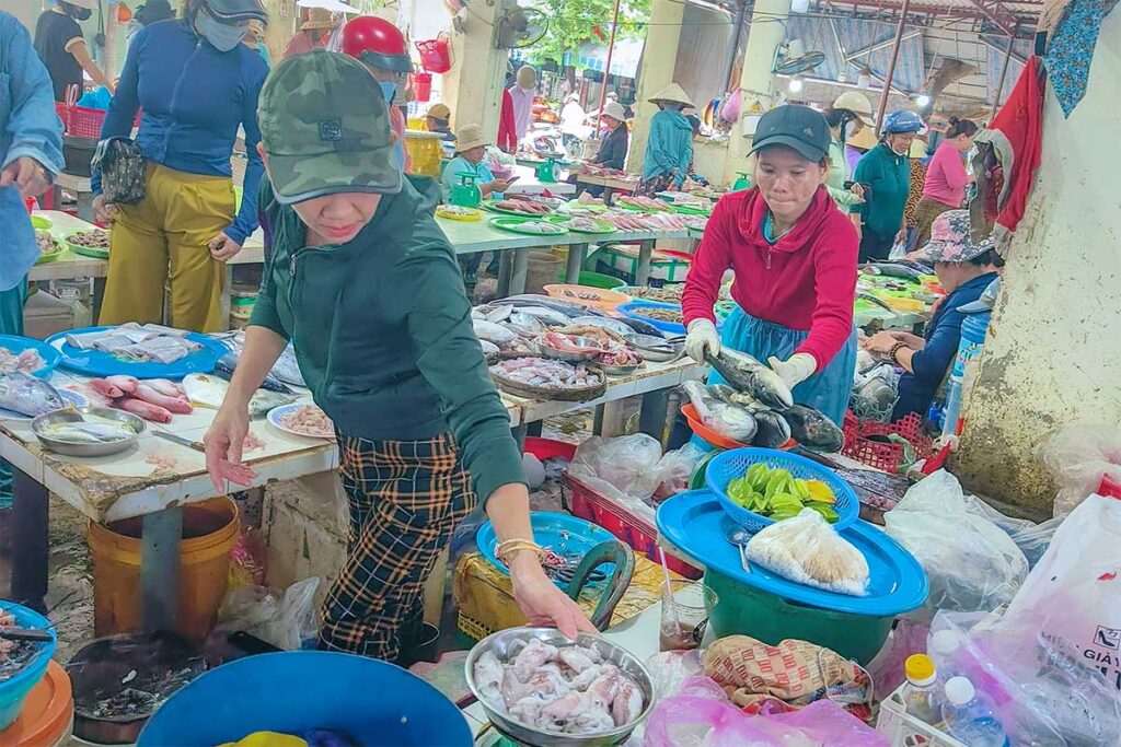Busy seafood section inside Tan An Market Hoi An with vendors selling fresh fish and squid on tables