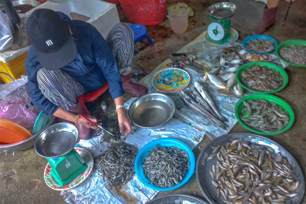 Seafood stall at Tan An Market Hoi An where a vendor prepares shrimp and displays fresh fish for sale.