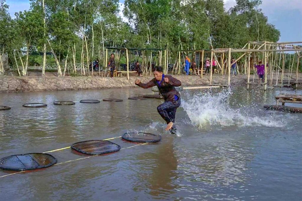 Folk games at Tan Lap Floating Village: visitor running across floating discs in a muddy pond, Long An