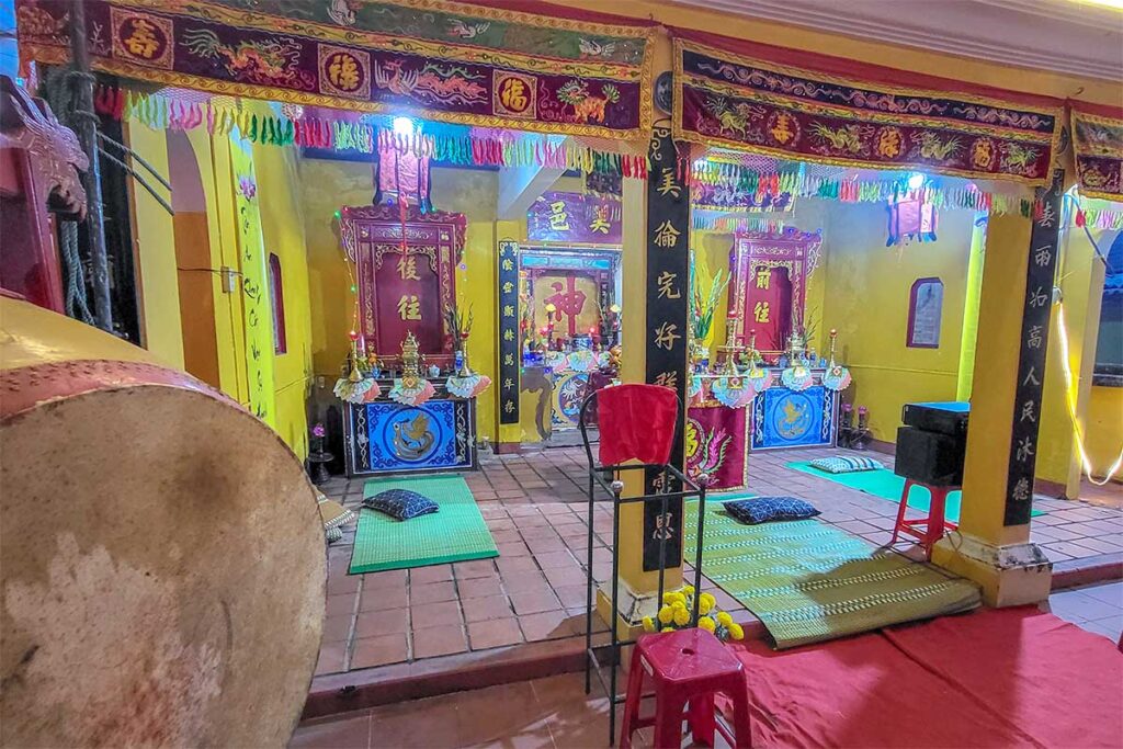 Colorful interior of Ong Cop Temple at Tan An Market Hoi An with altars, red banners, and worship offerings.