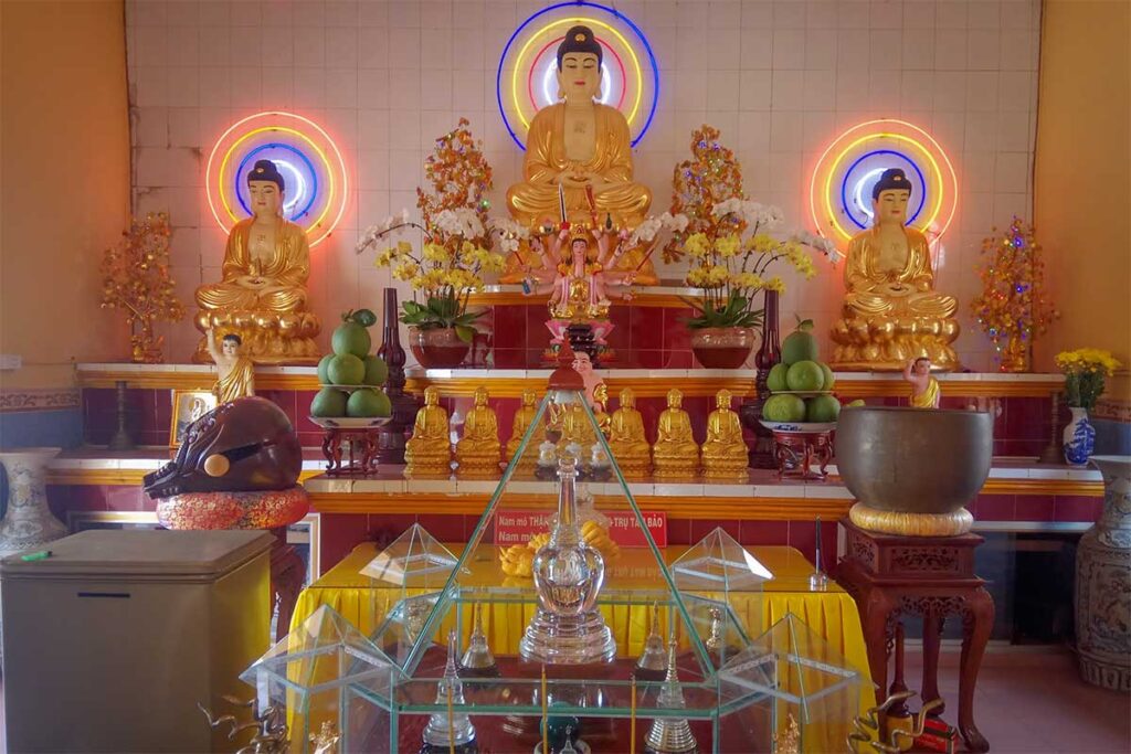Interior altar with golden Buddha statues and offerings at Van Phuoc Pagoda, Ben Tre