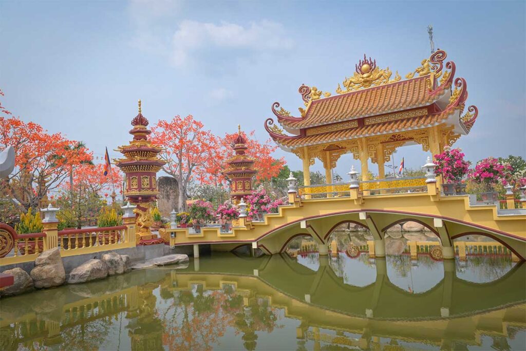 Ornate bridge over lotus pond with golden pavilion at Van Phuoc Pagoda, Ben Tre