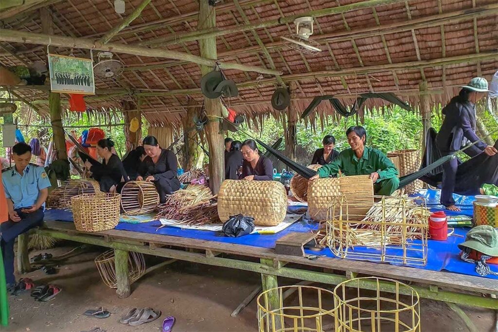 Traditional basket weaving in Xeo Quyt Forest – Men and women crafting bamboo baskets under a rustic shelter.