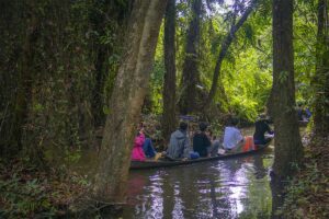 Tourists on a sampan in Xeo Quyt Forest – Visitors gliding along a narrow canal under the forest canopy.