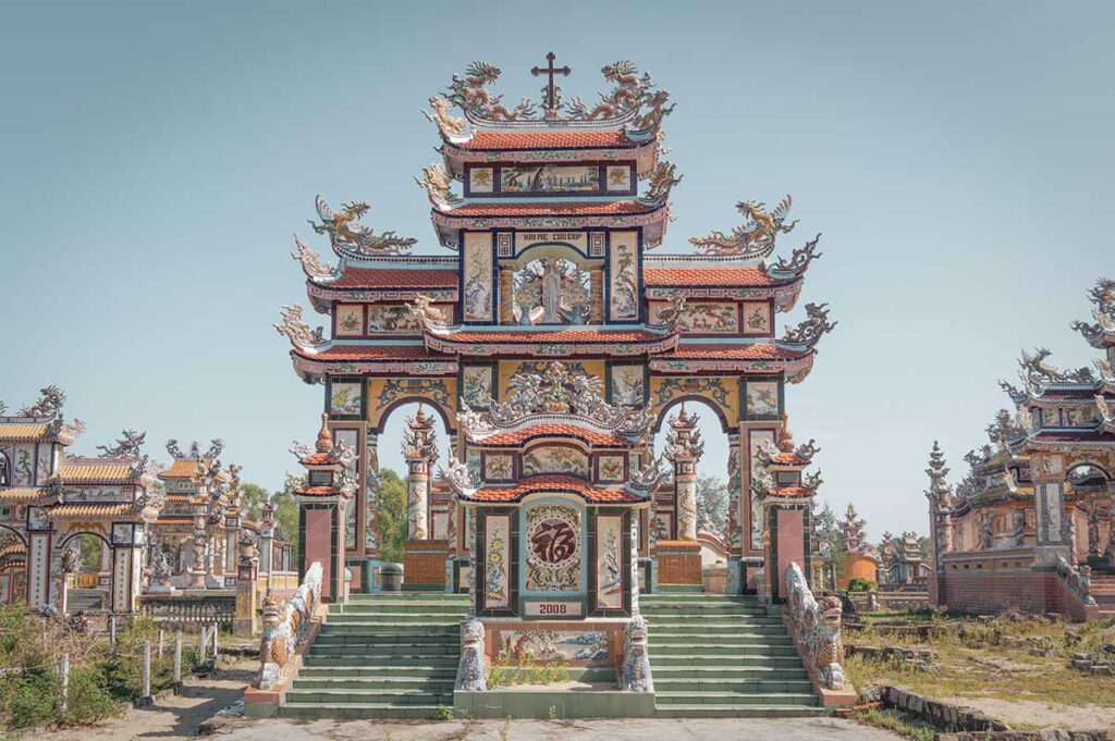 Front view of an elaborate family tomb at An Bang Cemetery near Hue, with dragon statues, ceramic mosaics, and multi-tiered roofs gleaming under the sun.