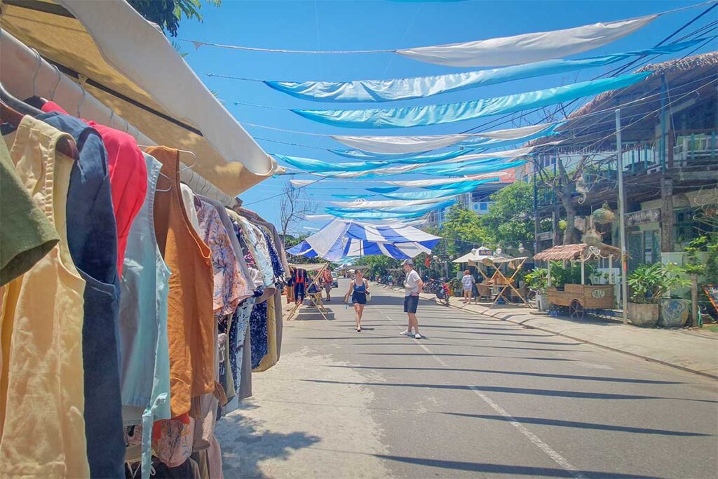 Street in An Bang Village near Hoi An lined with boutique shops and beach cafes under blue fabric shades.