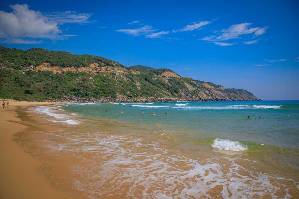 Visitors swimming in the turquoise water of Bai Mon Beach surrounded by forested cliffs in Phu Yen, Vietnam.