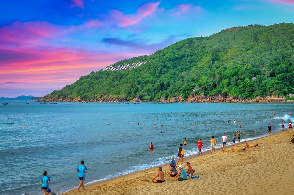 Sunset swimming at Quy Nhon City Beach, Vietnam, with locals and travelers in the water and the Ghenh Rang hillside behind—capturing the everyday vibe of the best beaches in Quy Nhon.