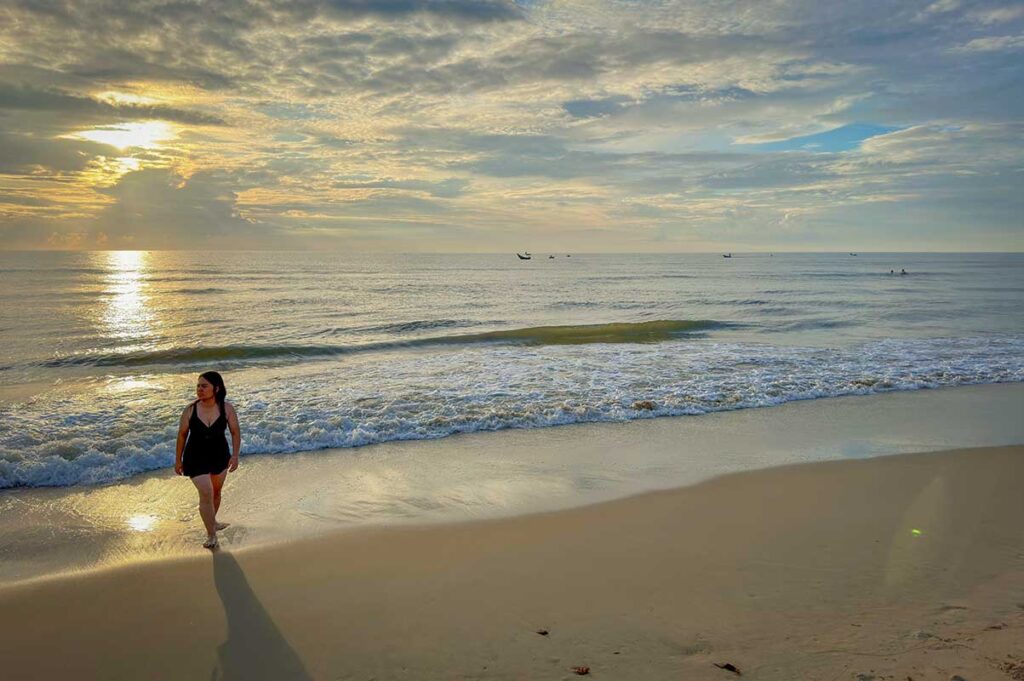 Traveler walking along Binh Minh Beach at sunrise, enjoying the quiet coastline and gentle waves of this hidden beach south of Hoi An.