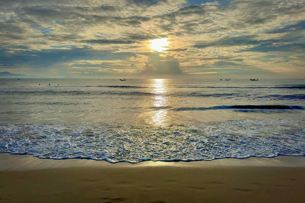 Sunrise over Binh Minh Beach near Hoi An, with calm waves and fishing boats silhouetted on the horizon — a peaceful early-morning view on Vietnam’s central coast.