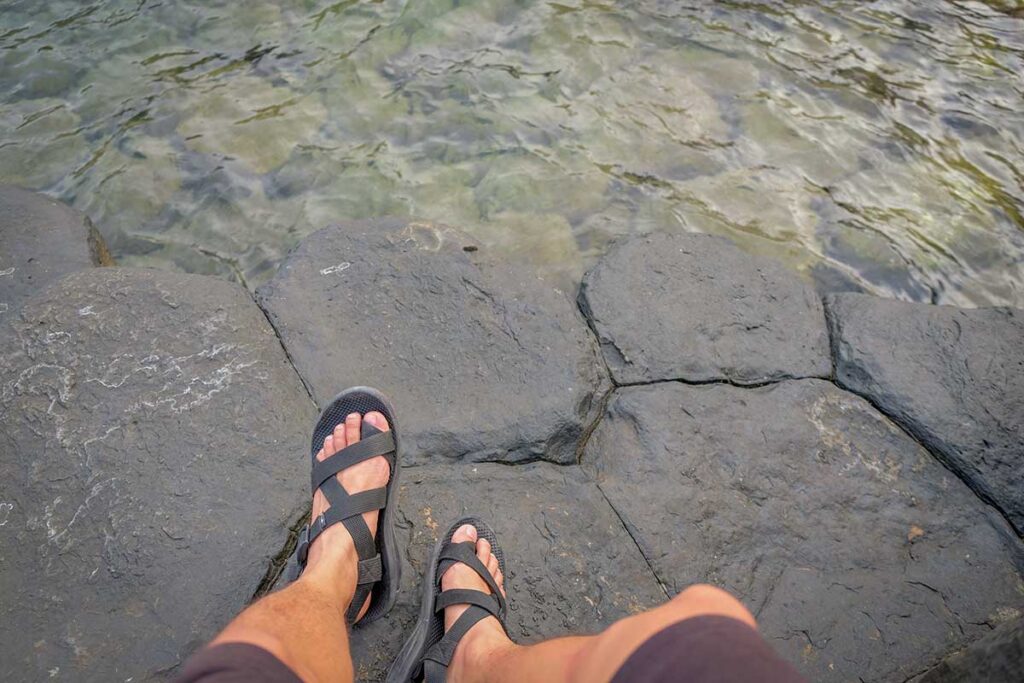 Close-up of a visitor sitting on the hexagonal basalt stones at Da Dia Reef in Phu Yen, Vietnam, with clear seawater below.