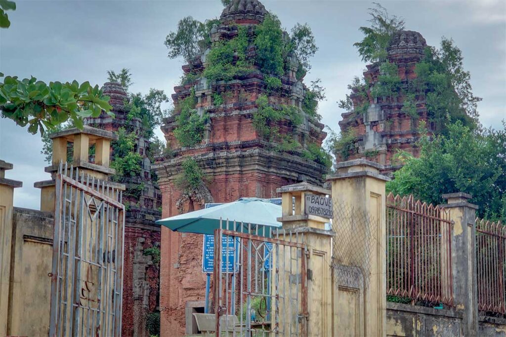 Entrance gate to Duong Long Cham Towers with ticket booth and the brick sanctuaries visible behind the fence.