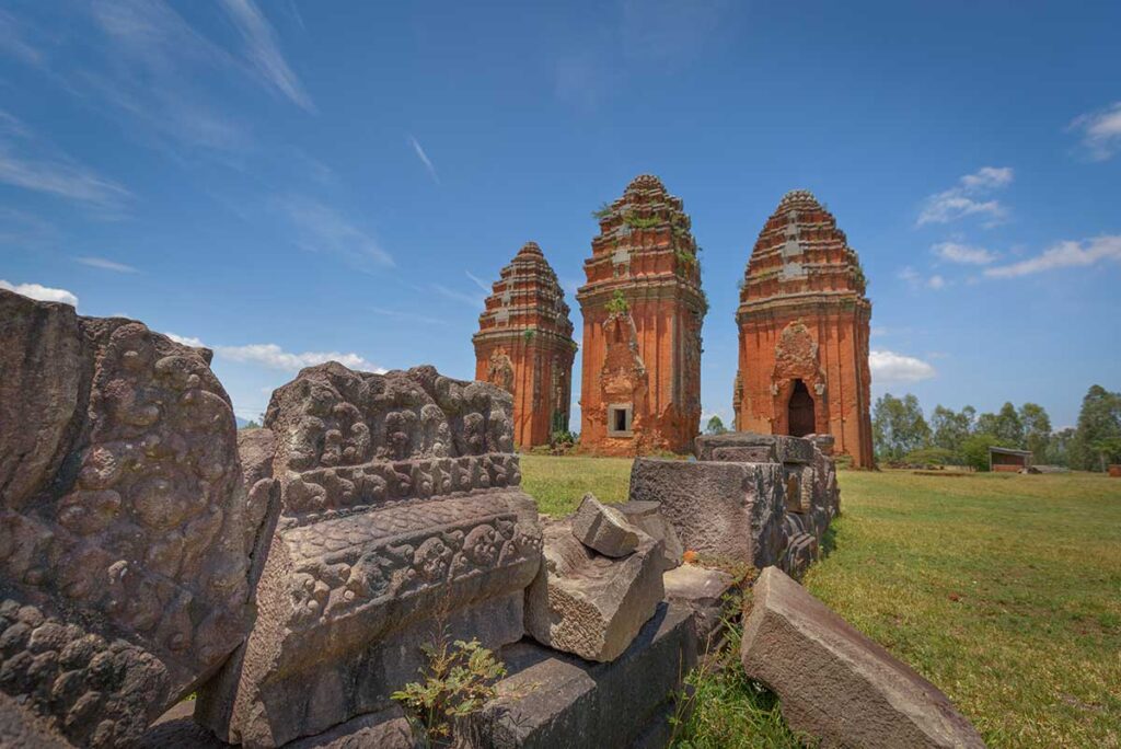 Stone relief blocks in front of the Duong Long Cham Towers, decorated with floral and geometric Cham motifs.