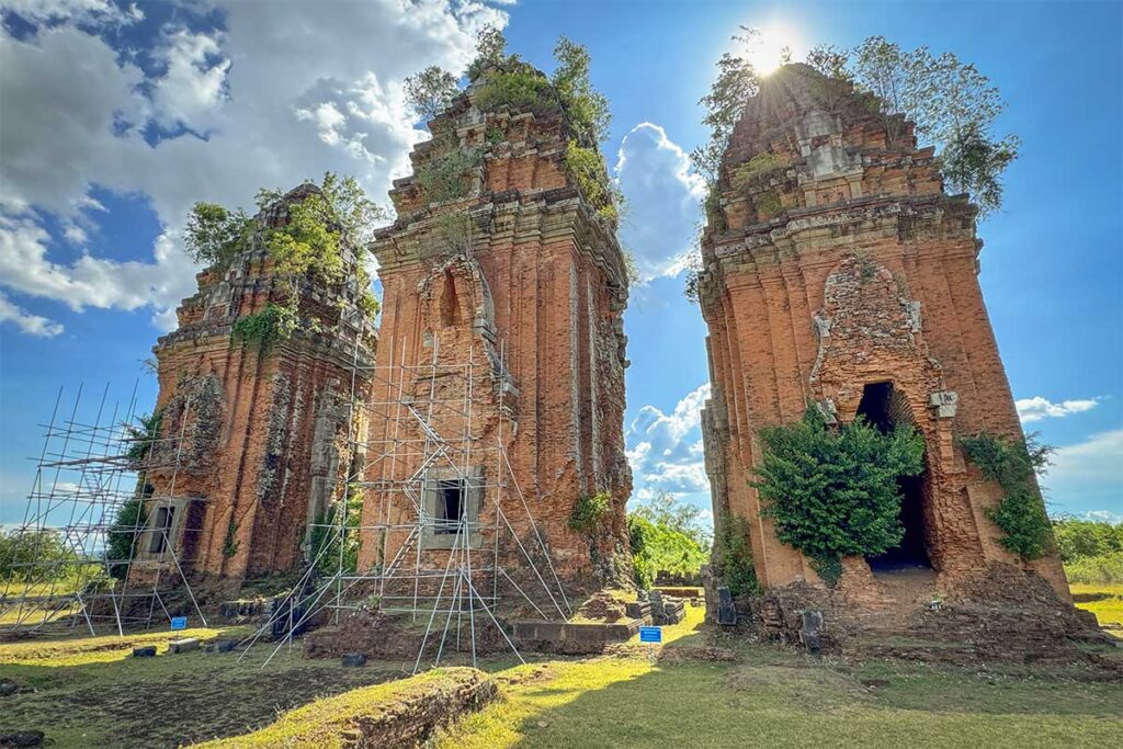 The three Duong Long Cham Towers with scaffolding for ongoing restoration, showing their monumental height and fragile condition.