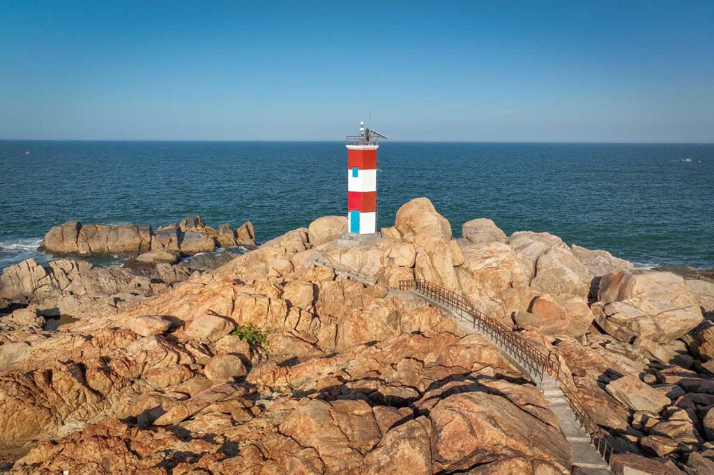 Red and white striped Ganh Den Lighthouse on the rocky coast near Da Dia Reef, Phu Yen Province, Vietnam.