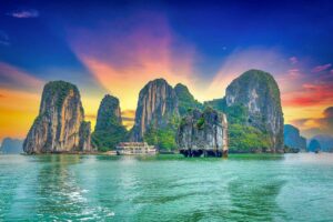 Halong Bay tours – Local Vietnam | cruise boat sailing between limestone karsts at sunset on Vietnam’s UNESCO World Heritage bay