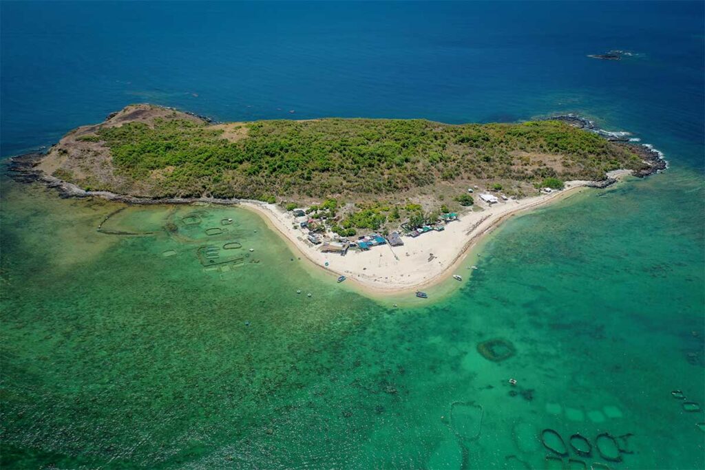 Aerial view of Hon Chua Island off the coast of Phu Yen, showing green hills, sandy beaches, and coral reefs visible through clear blue water.