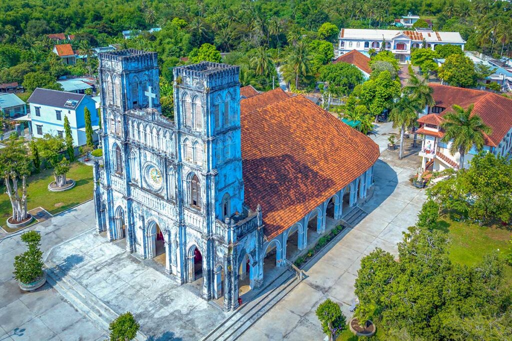 Aerial view of Mang Lang Church in Tuy An, Phu Yen, showing its Neo-Gothic façade, red-tiled roof, and surrounding village greenery.