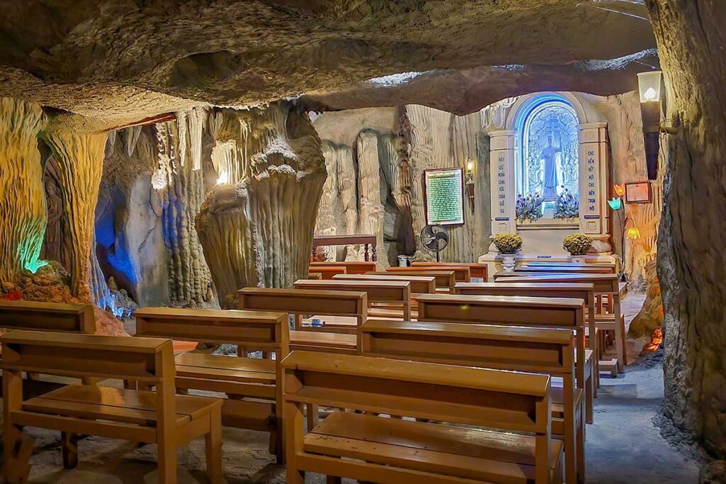 Interior of the artificial cave at Mang Lang Church, Phu Yen, with stone-like walls, wooden benches, and a lit altar for prayer.