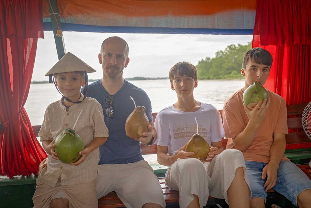 Family with children drinking fresh coconuts during a Mekong Delta boat tour, a refreshing activity for kids and parents alike.