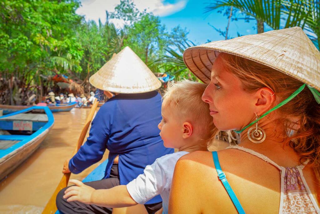 Mother holding her toddler on a traditional sampan ride through the palm-lined canals of the Mekong Delta, a gentle family activity.