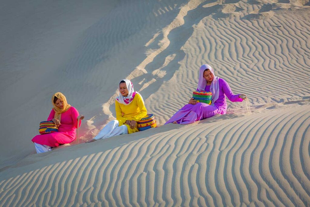 Cham women in traditional dress sitting on Nam Cuong Sand Dunes with woven baskets, Ninh Thuan