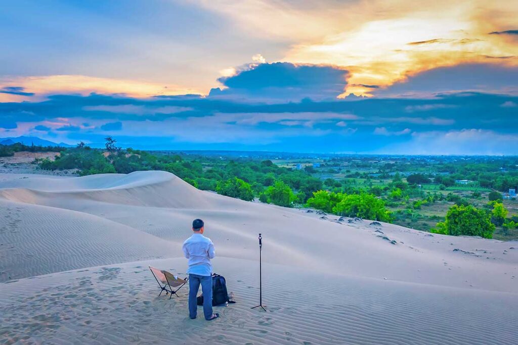 Traveler setting up camera tripod on Nam Cuong Sand Dunes overlooking Phan Rang countryside