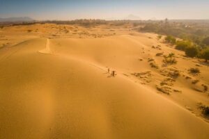 Mother and child walking across Nam Cuong Sand Dunes with baskets at sunrise, Ninh Thuan