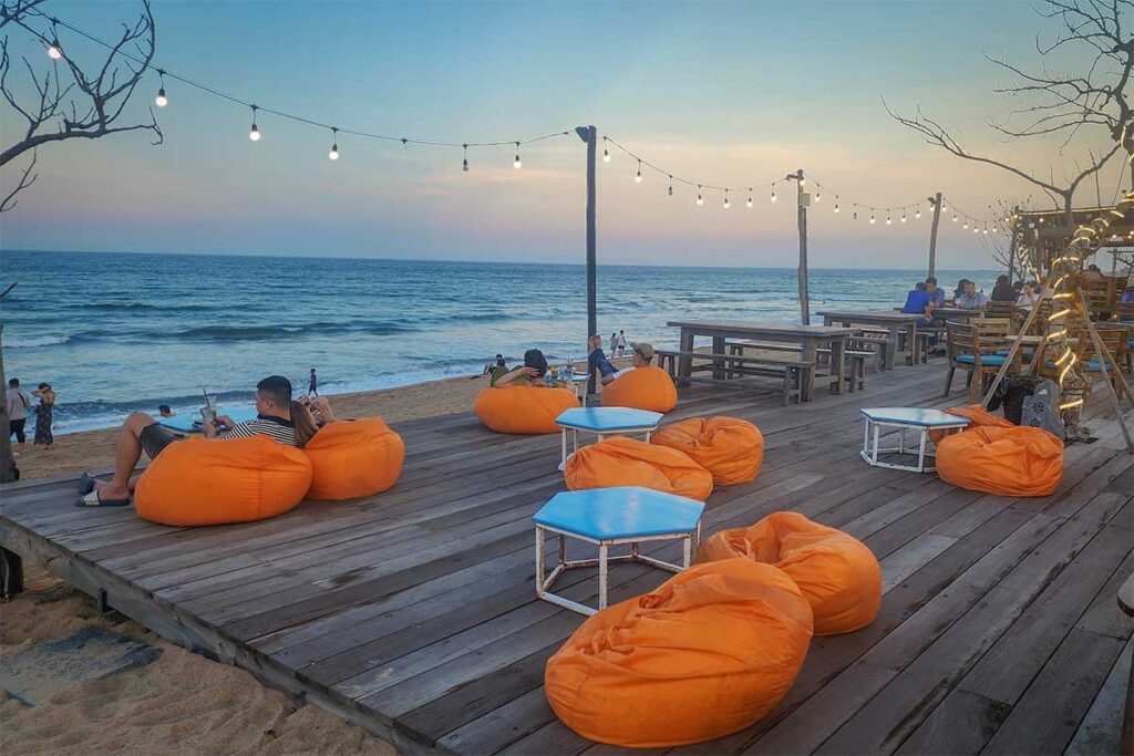 Beachfront café near Nghinh Phong Tower in Tuy Hoa with bean bag seating, wooden deck, and ocean views at sunset.