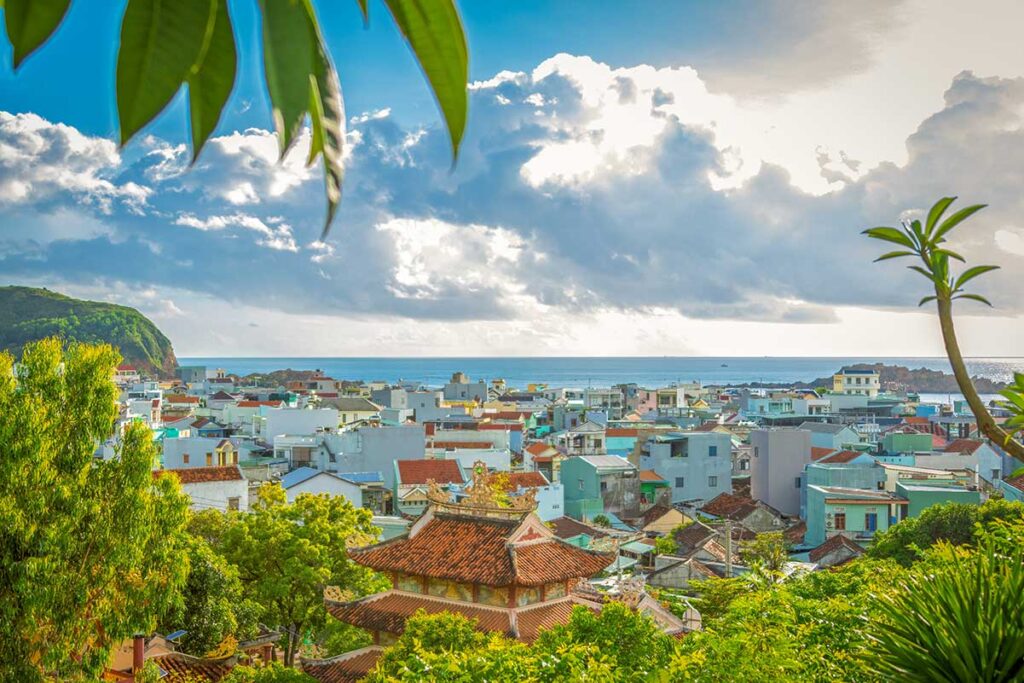View over Nhon Hai Fishing Village – A colorful mix of tiled rooftops and houses with the South China Sea in the background, seen from a hillside above the village.