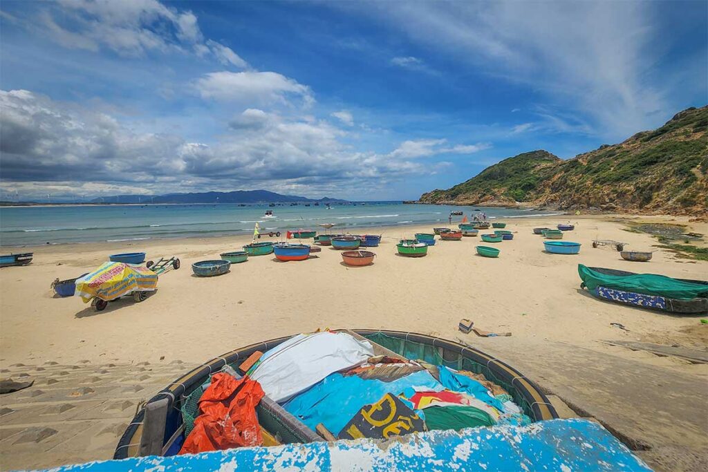Nhon Ly Beach cove on the Phuong Mai Peninsula: coracle (basket) boats pulled up on golden sand beside a rocky headland—classic working beach near Quy Nhon, Vietnam.