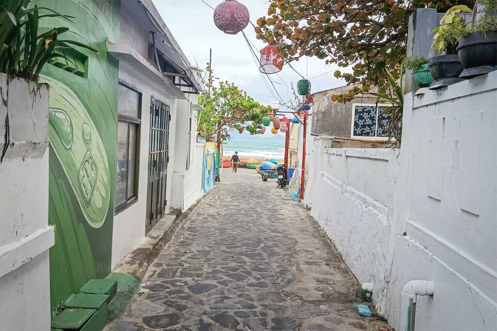 Cobblestone alley in Nhon Ly fishing village, Quy Nhon, with sea-themed murals leading to the beach and basket boats.