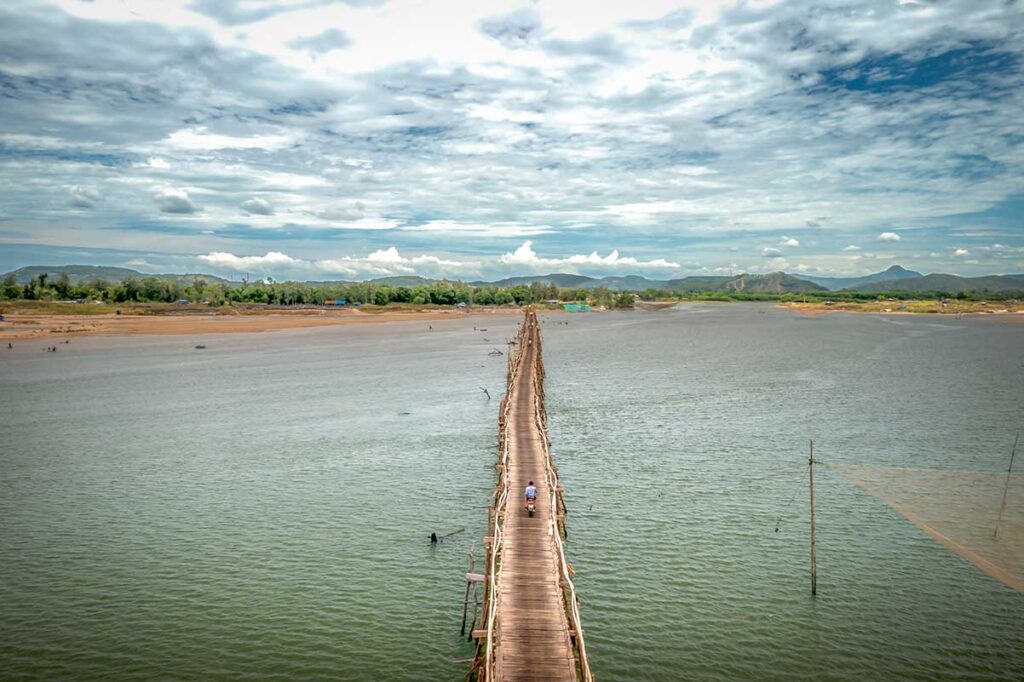 Drone shot of Ong Cop Wooden Bridge stretching across the wide Da Rang River in Phu Yen, surrounded by mountains and open water.
