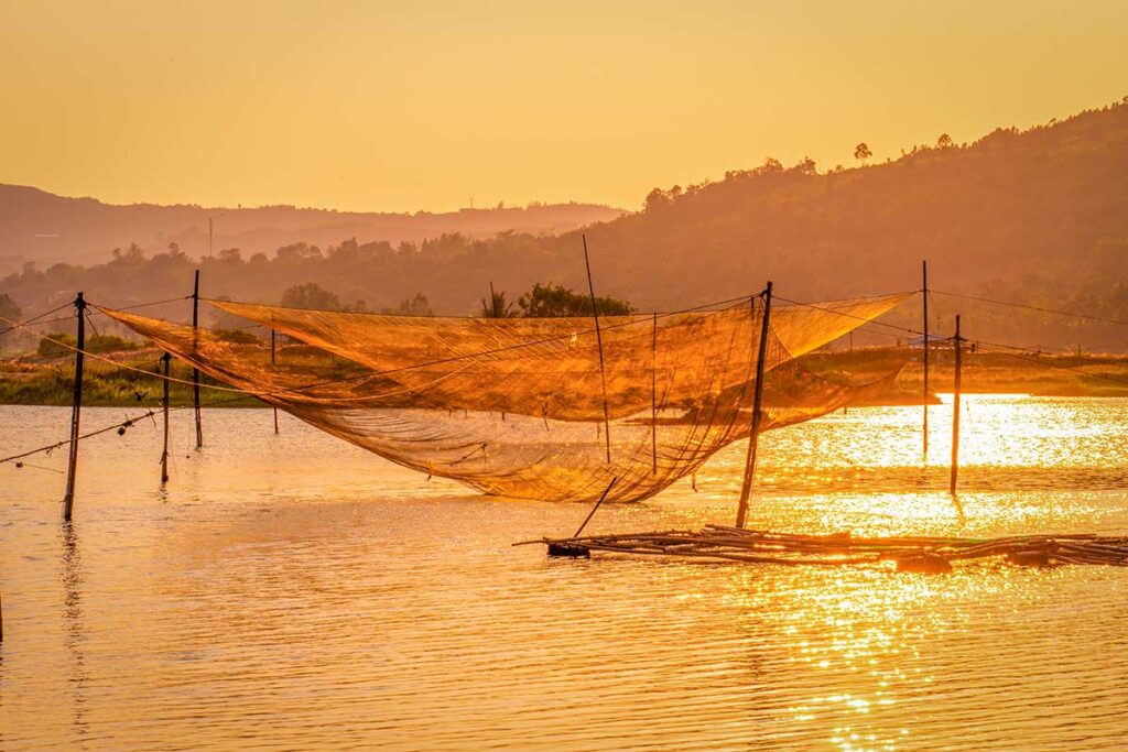 Fishing nets at sunset near Ong Cop Wooden Bridge, Phu Yen, casting golden reflections across the Binh Ba River.