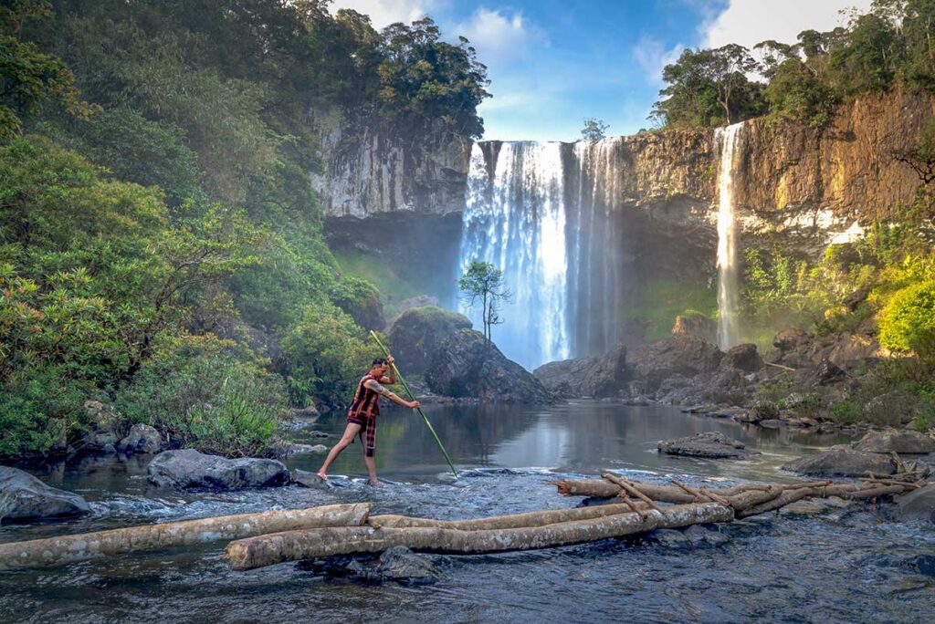 Pleiku tours – Local Vietnam | local man standing near a powerful waterfall surrounded by forest in Pleiku, Central Highlands Vietnam
