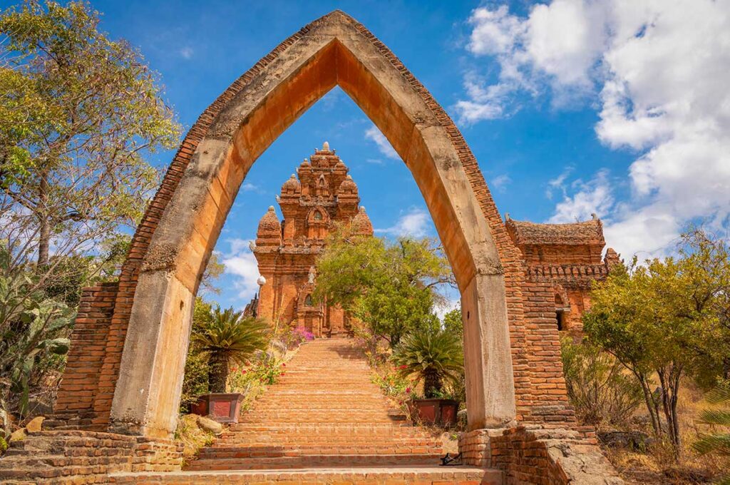 Stone arch and stairway leading up to Po Klong Garai Tower in Phan Rang, Vietnam, framed by trees and blue sky.
