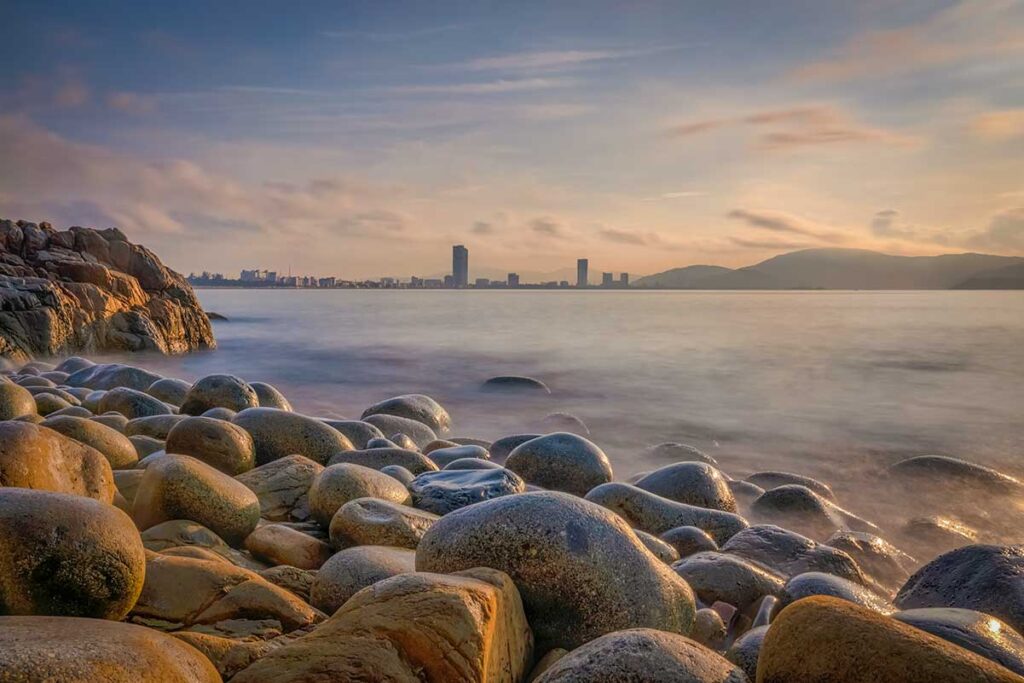 Queen’s Beach, Quy Nhon: smooth “egg” stones at dusk with the city skyline across the bay.