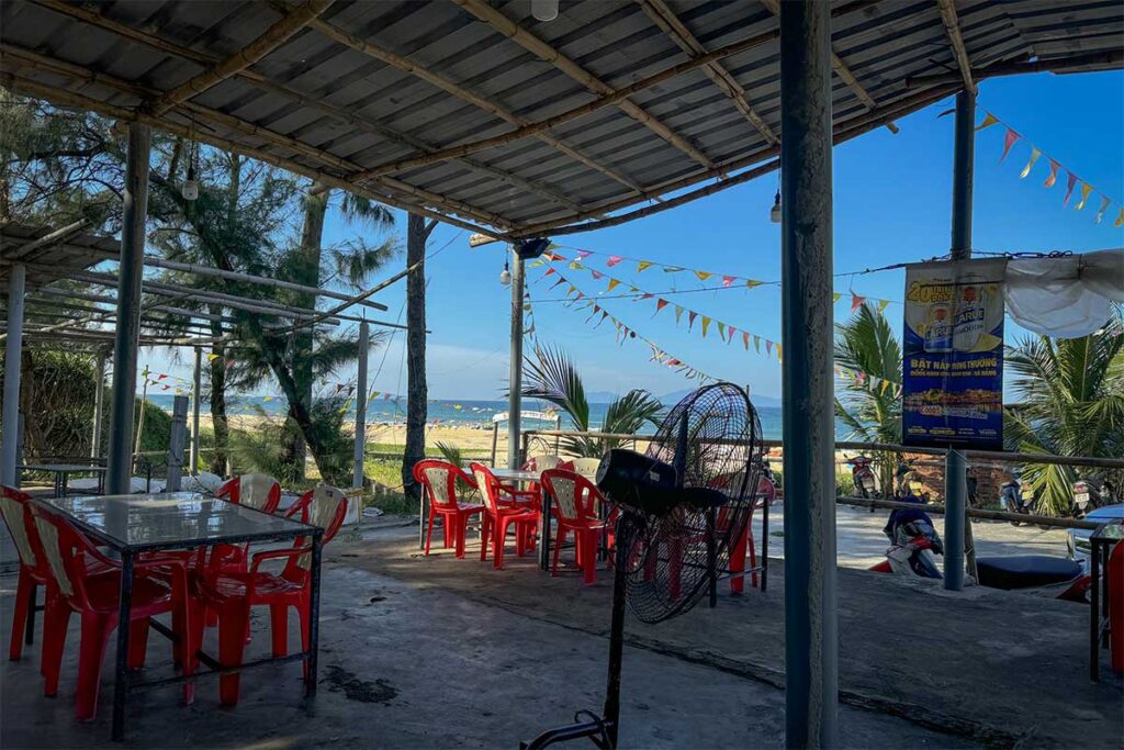Simple beachfront seafood shack at Binh Minh Beach with red plastic chairs and ocean views, serving fresh local dishes by the water.