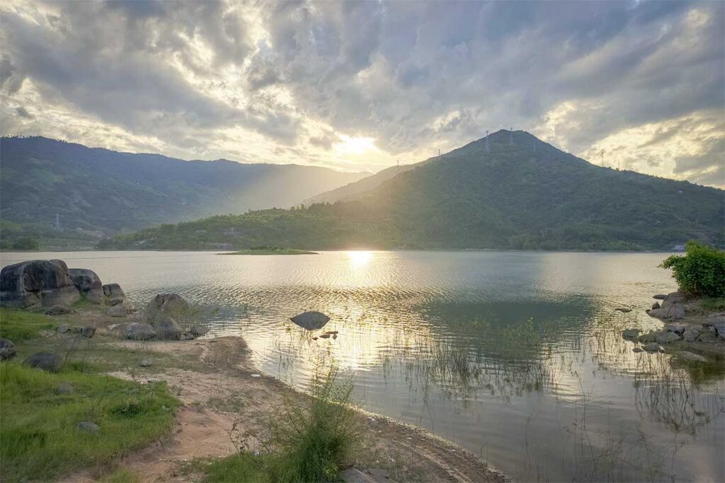 Sunset view over Suoi Dau Lake at the base of Hon Ba Mountain, surrounded by rolling hills and calm water – a scenic starting point for the Hon Ba Nature Reserve road trip.